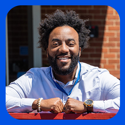 Market People Partner Anthony Agnew smiling in the sun with the brick of the Walmart Home Office behind him.