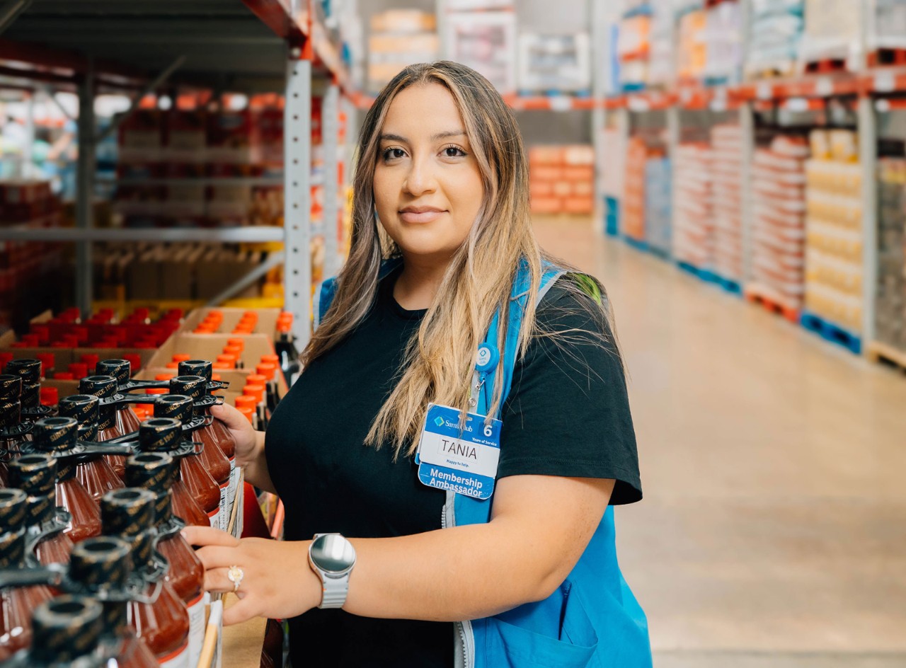 Sam’s Club associate Tania Gramajo looks up at camera while tidying shelves.