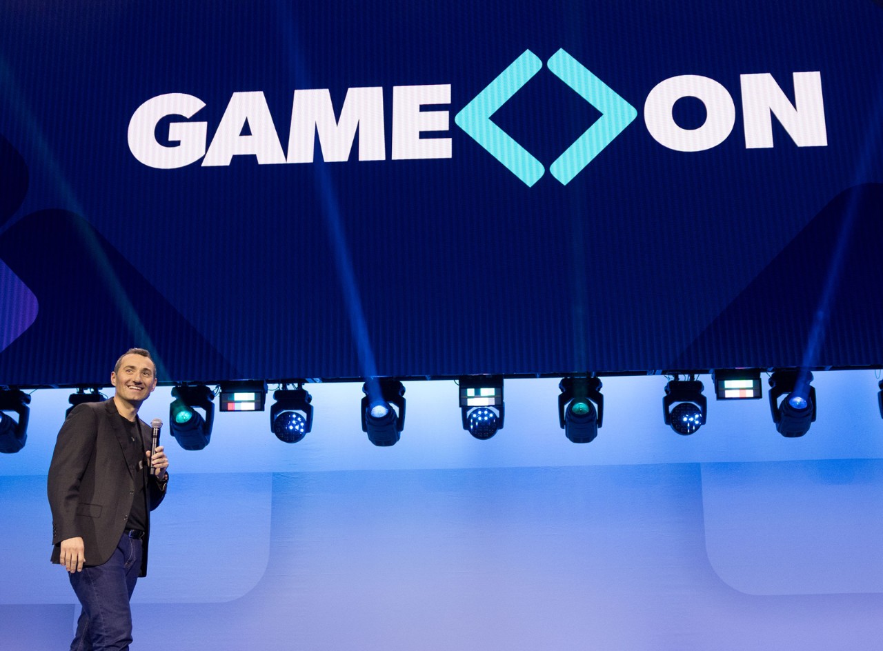 Chris smiles at associates in the audience at the Sam’s Club meeting with the words “Game On” appearing on the screen above.